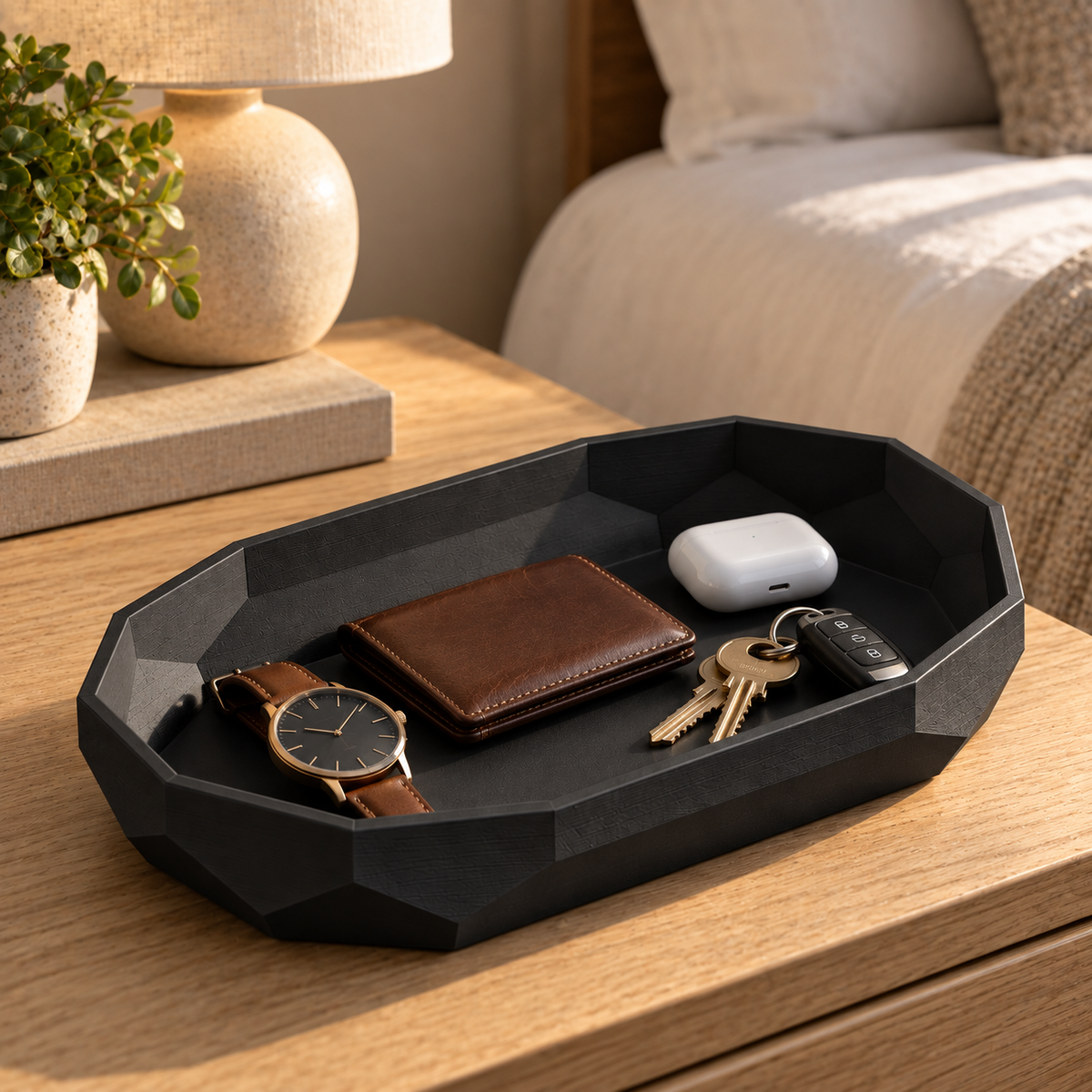 Facet Oval Catch-All Tray in Matte Black holding a watch, wallet, earbuds and keys on an oak nightstand