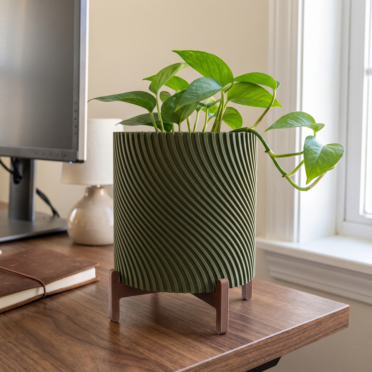 Twisted Planter with Stand in Moss Green holding a small pothos on a walnut desk beside a monitor