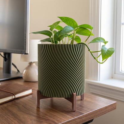 Twisted Planter with Stand in Moss Green holding a small pothos on a walnut desk beside a monitor