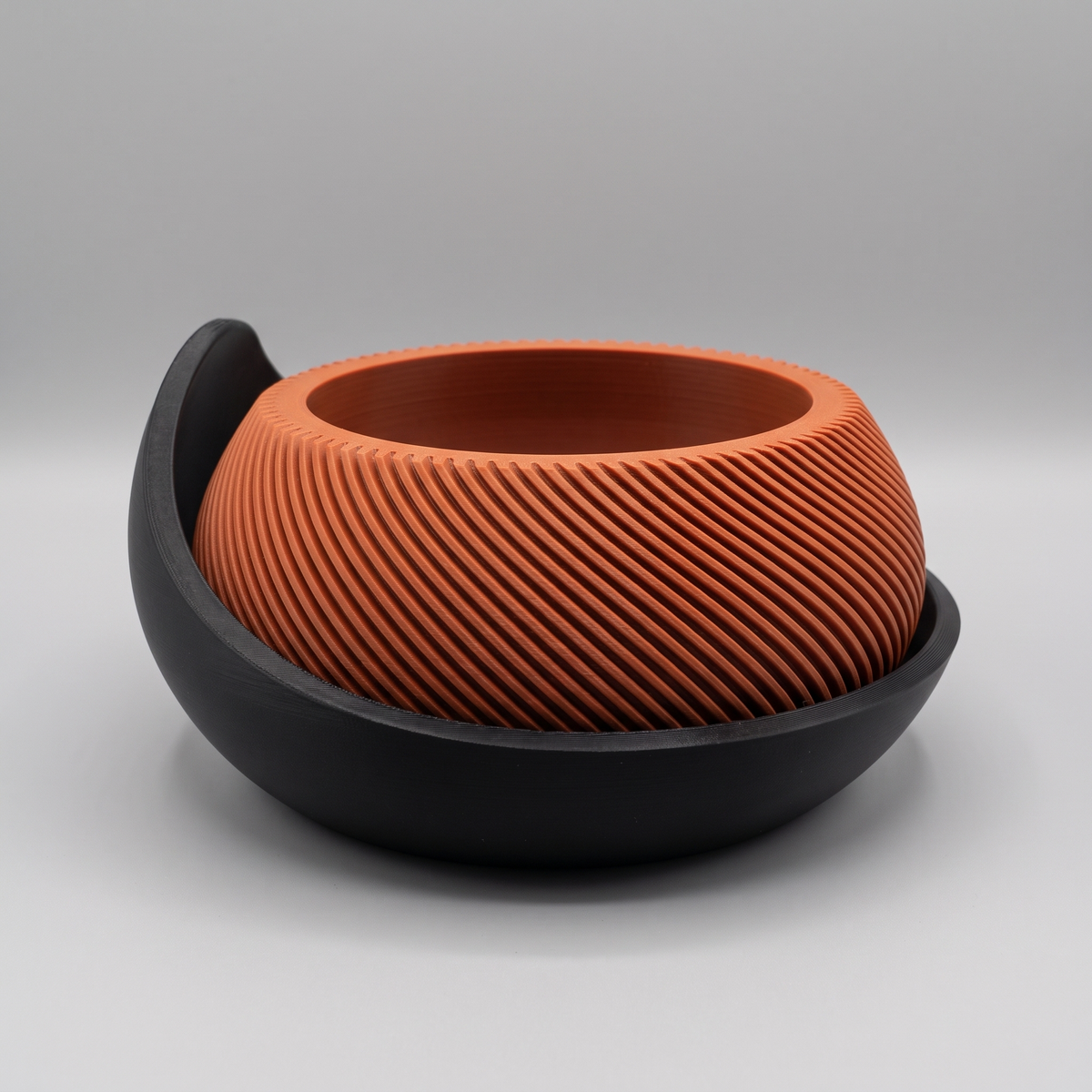 Swirl Ribbed Bowl Planter with Cradle Saucer in Burnt Rust with a Matte Black saucer, studio view on gray